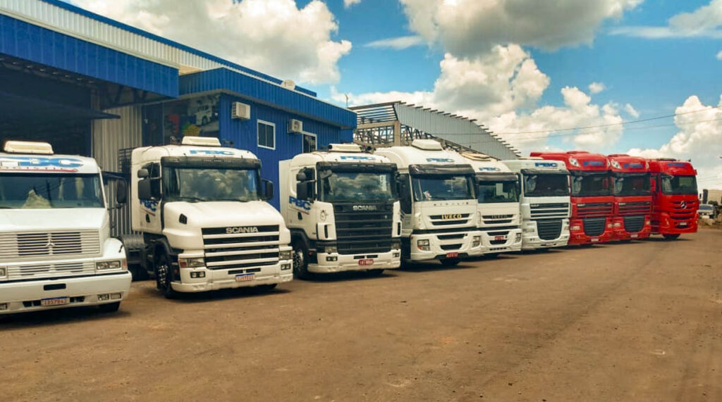 Frota de 10 caminhões estacionados em em frente pavilhão para carregamento de estraturas metalicas